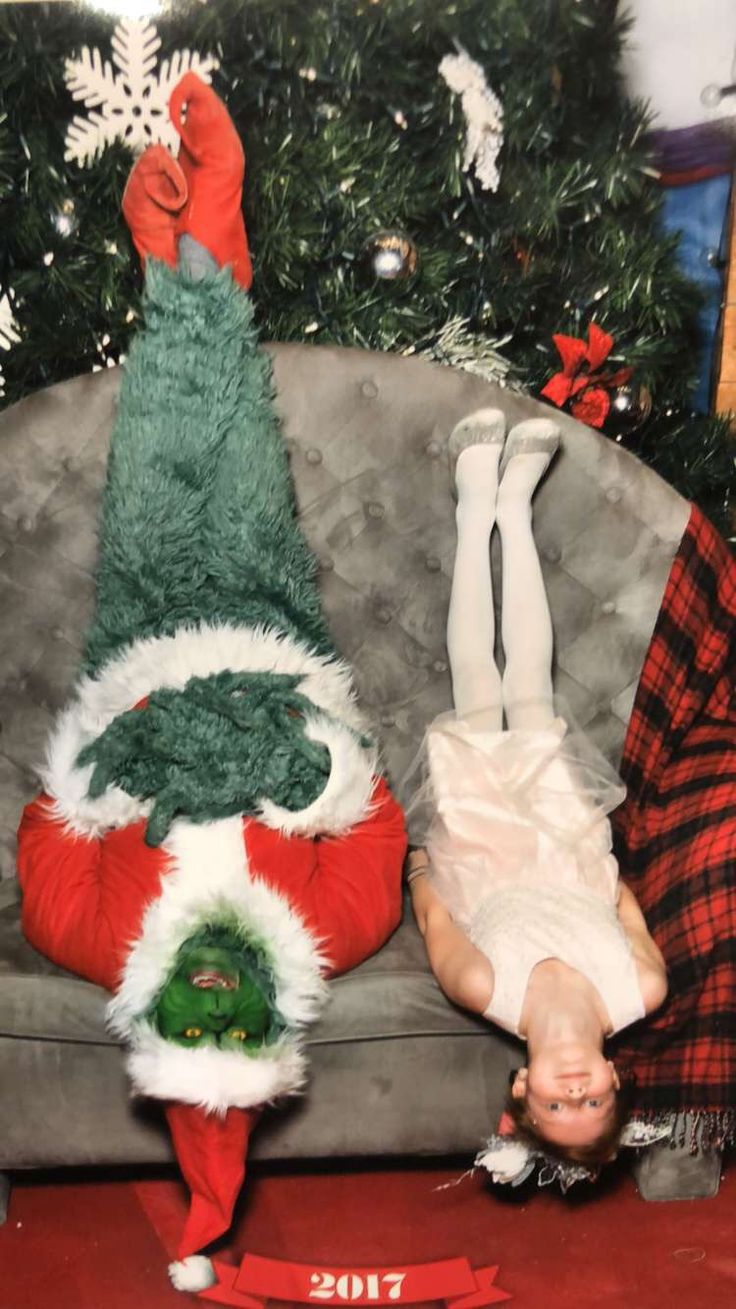 two people dressed up as santa clause laying on a couch in front of a christmas tree