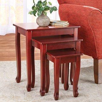 three wooden nesting tables on carpeted floor next to red chair and potted plant