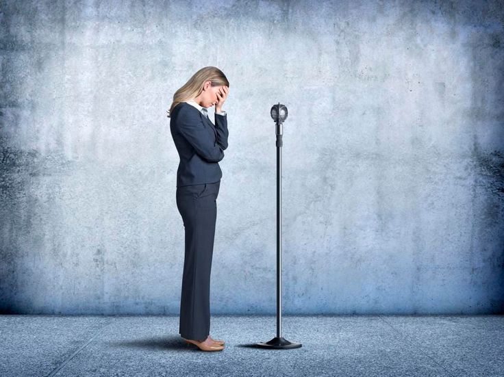 a woman standing in front of a microphone with her hand on her head and looking at the ground