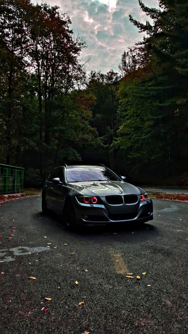 a black car parked on the side of a road in front of trees and clouds