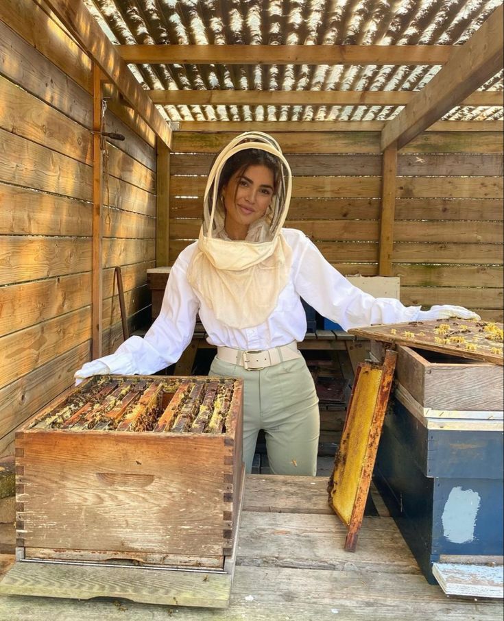 a woman wearing a beekeeper's outfit standing in front of some hive boxes