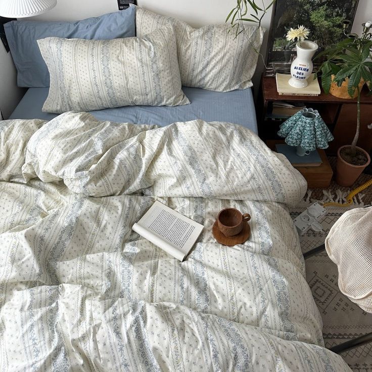 an unmade bed with blue and white comforter next to potted plants on a table