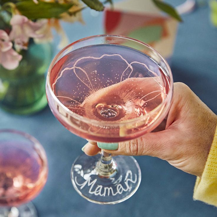 a person holding up a wine glass in front of two glasses filled with pink liquid