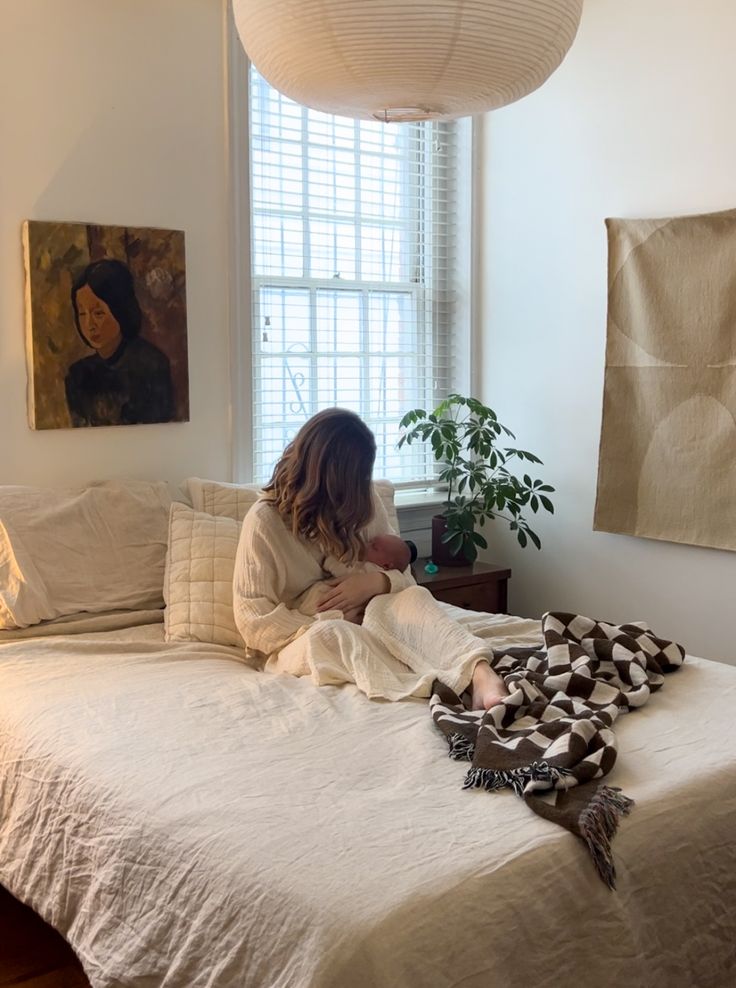 a woman sitting on top of a bed next to a potted plant in a bedroom