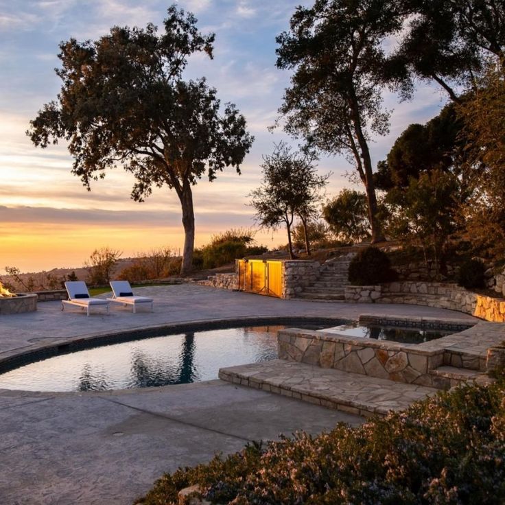 an outdoor swimming pool with lounge chairs and trees in the background at sunset or dawn