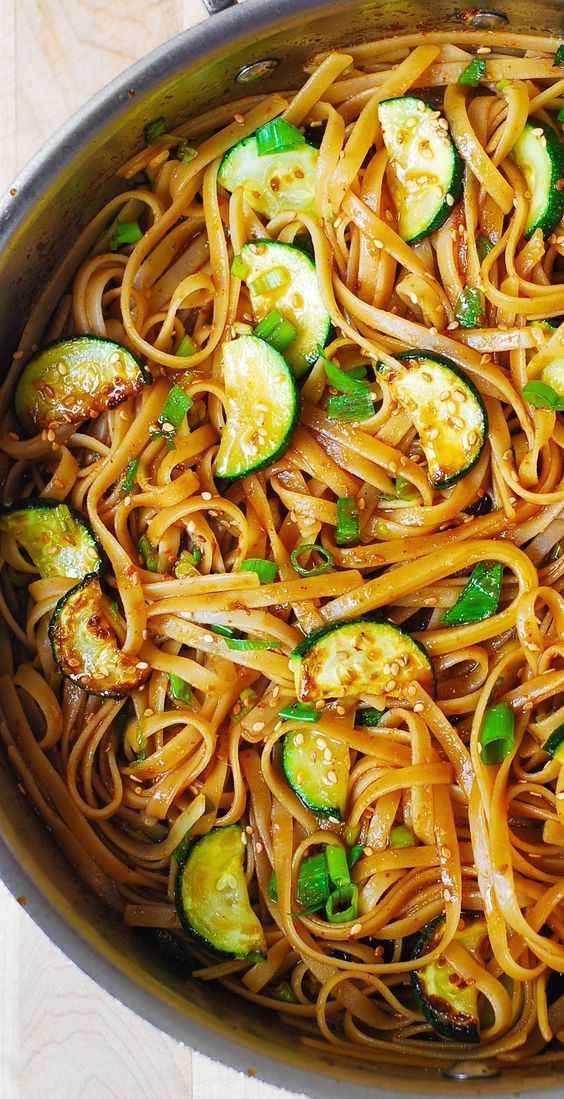 a pan filled with noodles and zucchini on top of a wooden table next to utensils