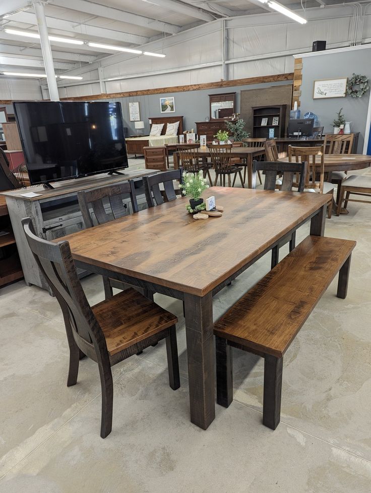 a table and benches in a store with chairs around it on the floor, next to a flat screen tv