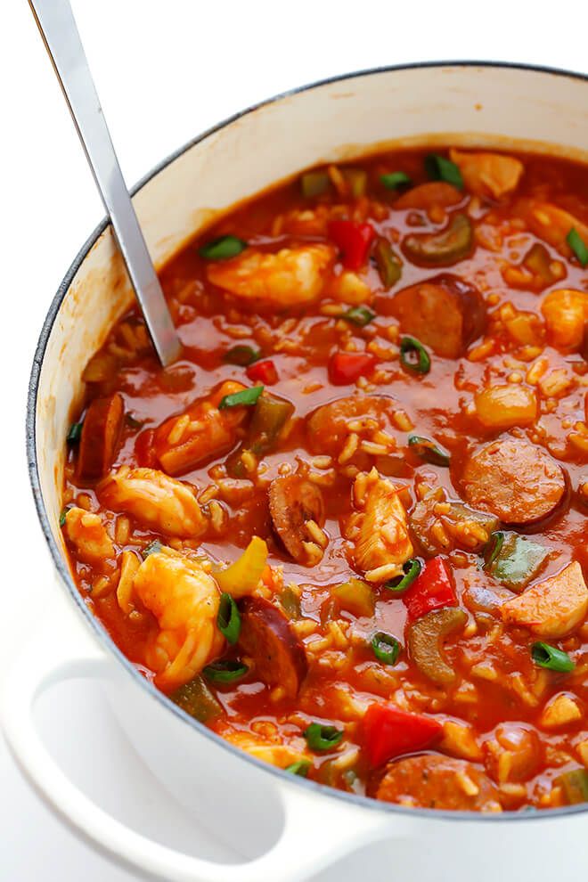 a large pot filled with lots of food on top of a white table next to a silver spoon