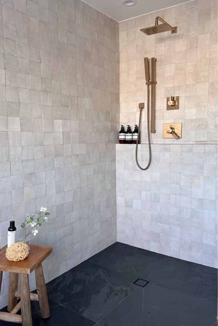 a white tiled bathroom with a wooden stool and shower head mounted to the wall next to it