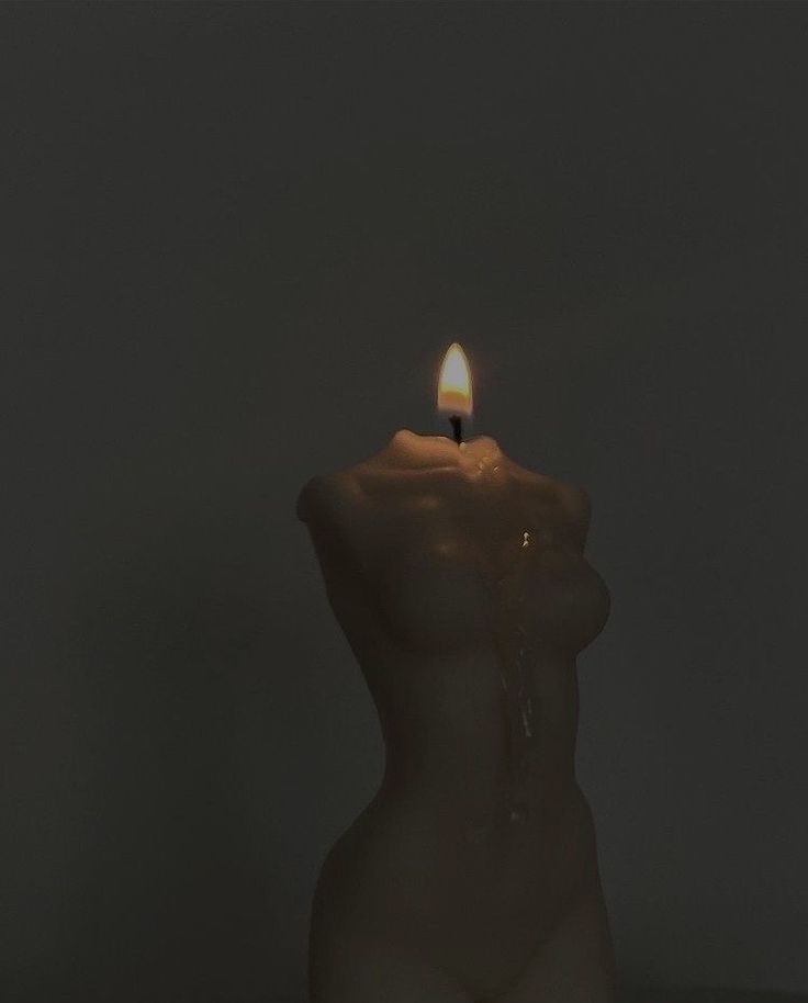 a lit candle in the shape of a woman's torso on a table against a dark background