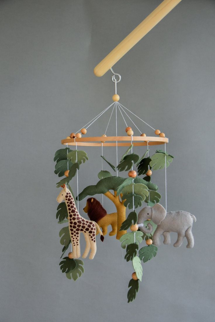 a mobile with animals hanging from it's sides and leaves on the bottom, in front of a gray wall