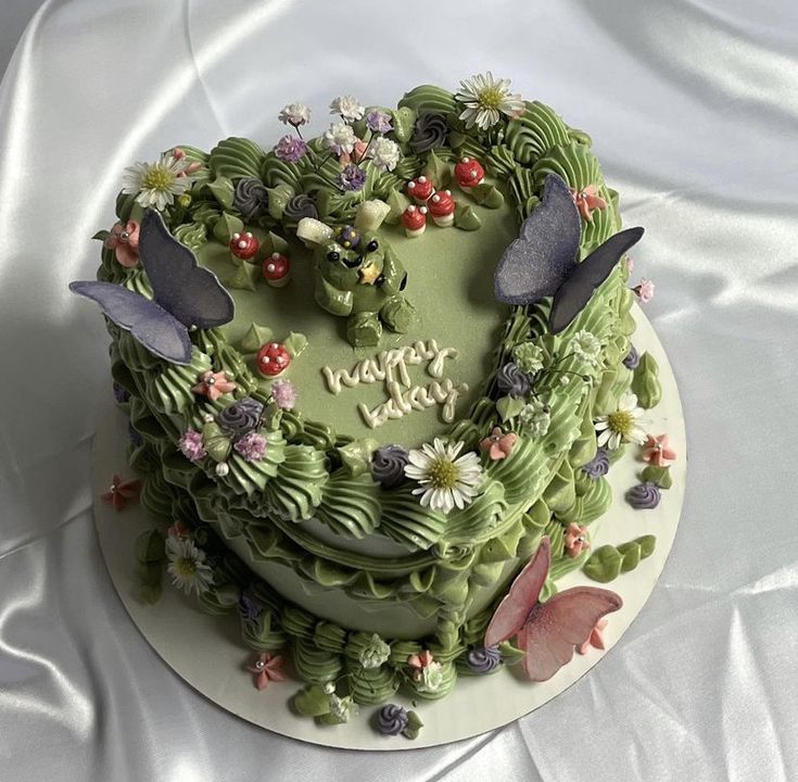 a heart shaped cake with flowers and butterflies on it's top, sitting on a white table cloth