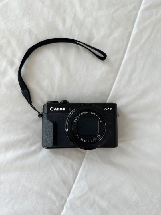 a black camera sitting on top of a white bed sheet with a strap around it's neck