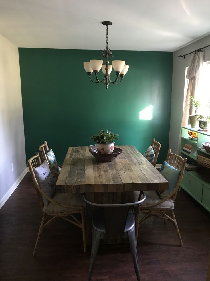 a dining room table with chairs and a potted plant on top of it in front of a green wall