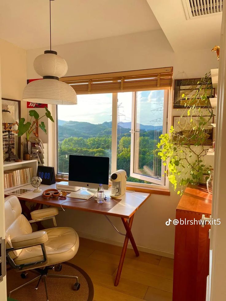 a desk with a computer on top of it in front of a window overlooking the mountains