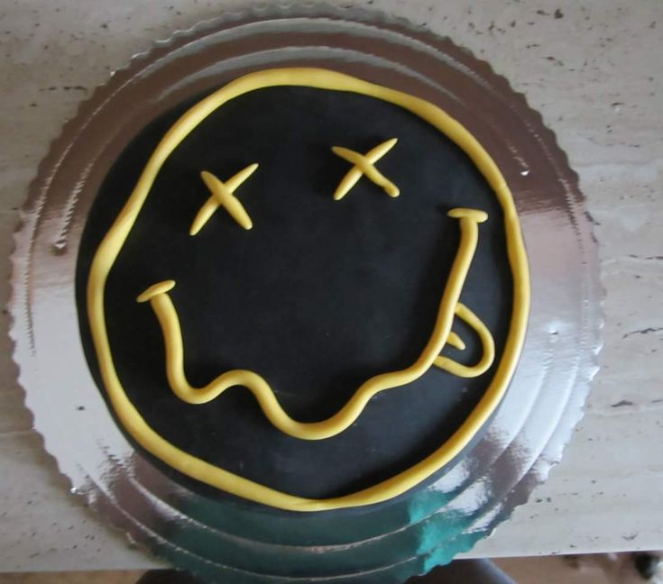 a black and yellow smiley face cake sitting on top of a metal plate with gold icing