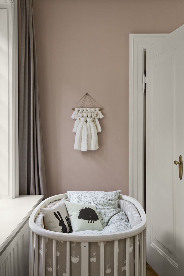 a white crib with pillows and blankets on it in front of a pink wall