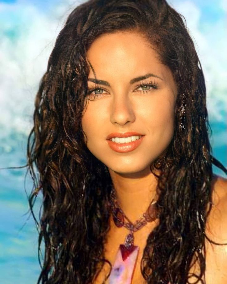 a beautiful young woman with long curly hair posing for a photo in front of the ocean