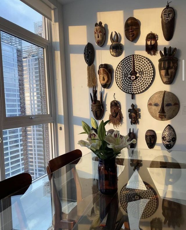 a dining room table with vases on the wall and african masks hanging on the wall