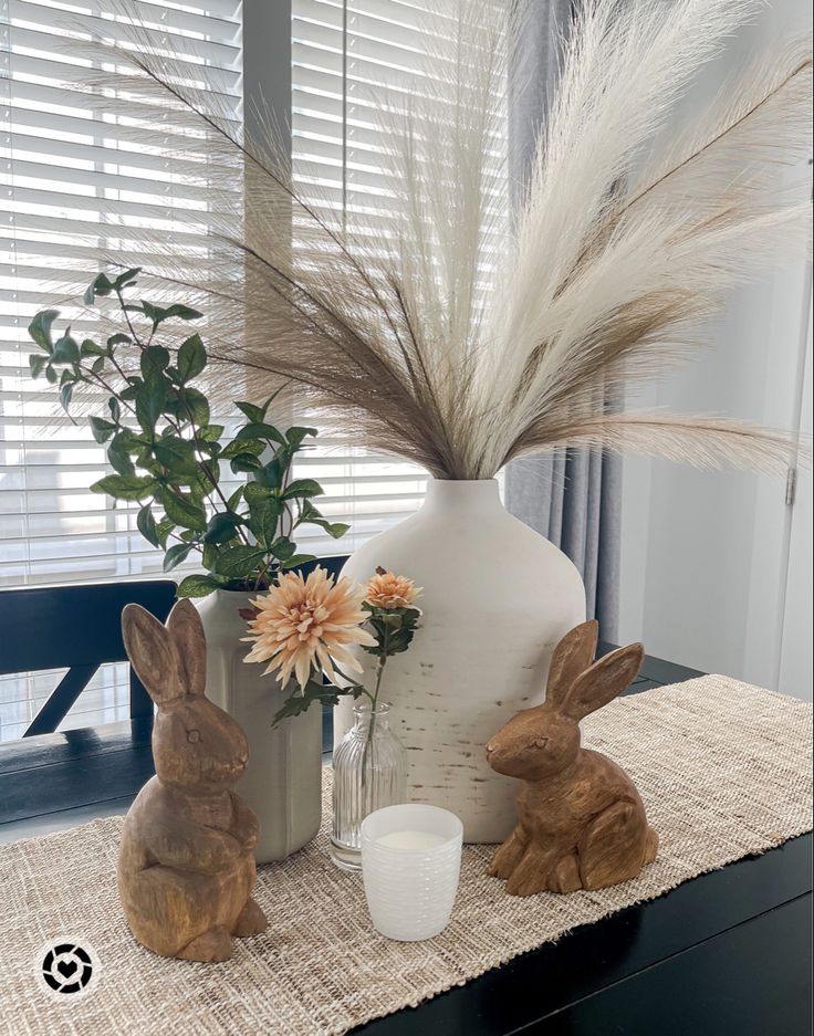 two bunny figurines sitting on a table next to a vase with flowers in it