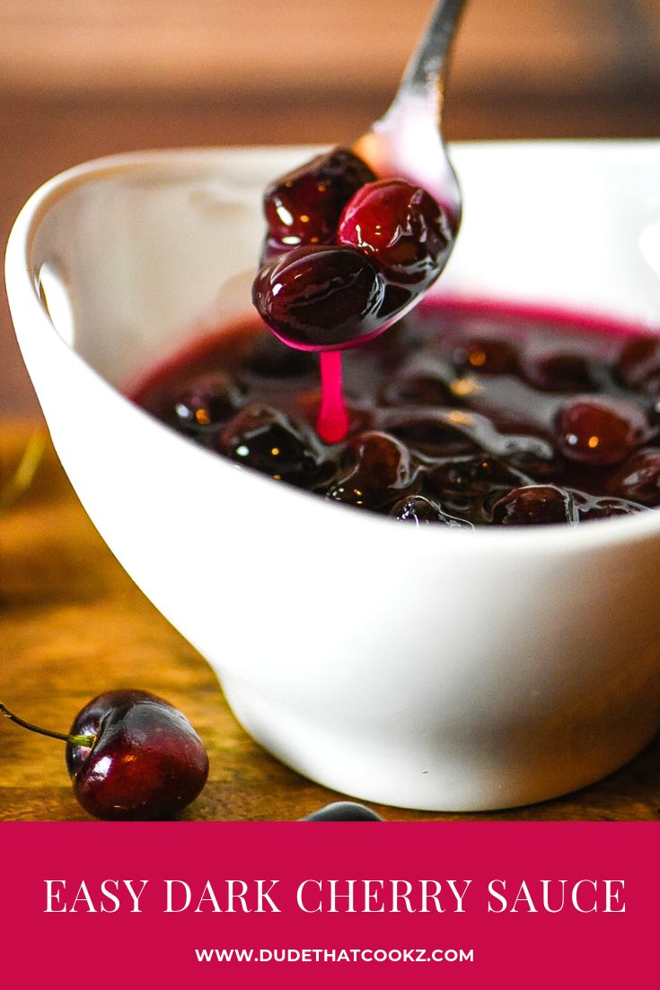 a white bowl filled with cherries on top of a wooden table next to a spoon