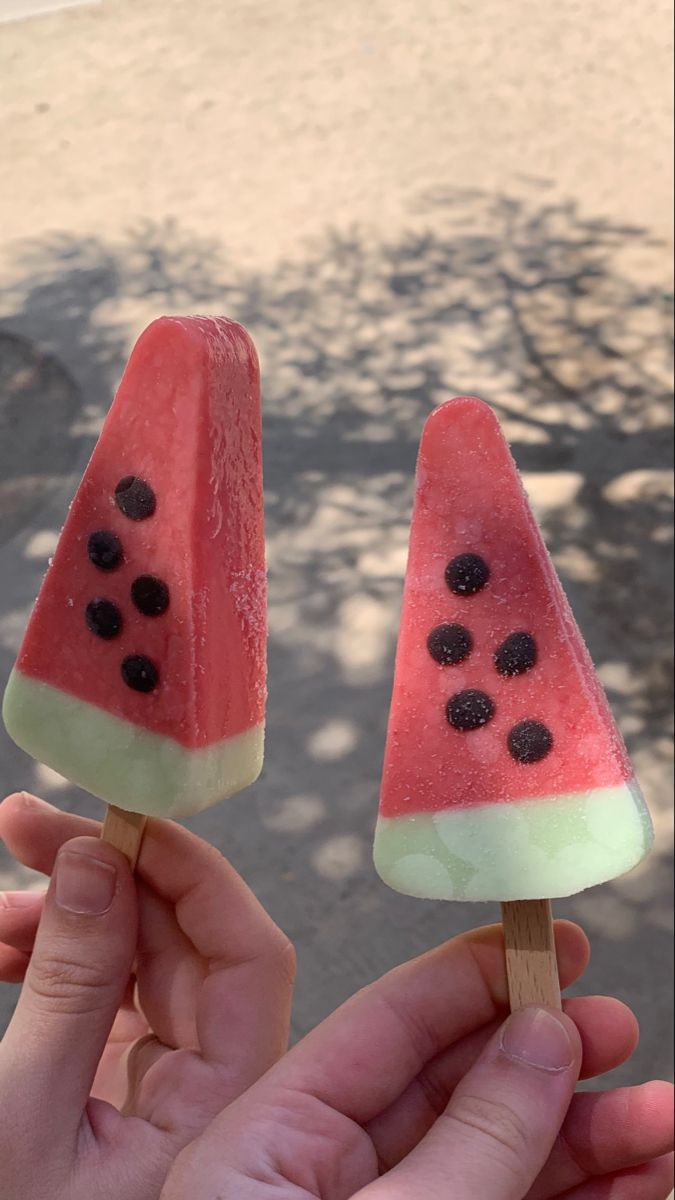 two popsicles with watermelon and blackberries on them are being held by someone's hand