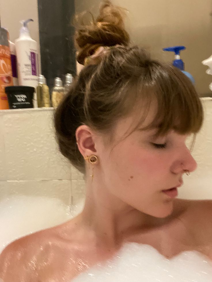 a woman sitting in a bathtub with soap on her head and hair pulled back