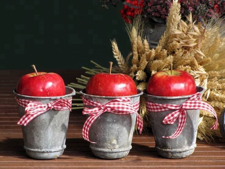 three buckets with apples tied to them sitting on a table next to some wheat