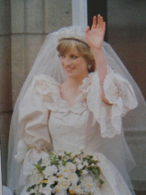 a woman in a wedding dress waves to the crowd