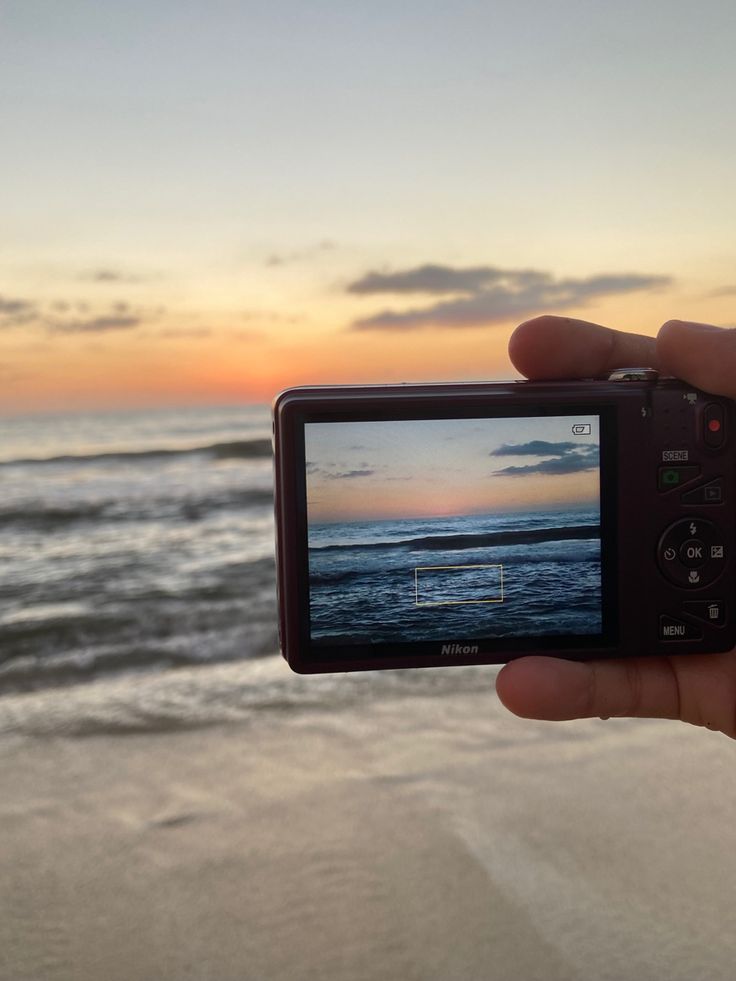 someone is holding up their camera to take a photo on the beach at sunset or sunrise