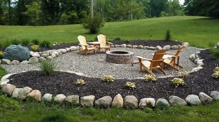 an outdoor fire pit surrounded by rocks and chairs in the middle of a grassy area