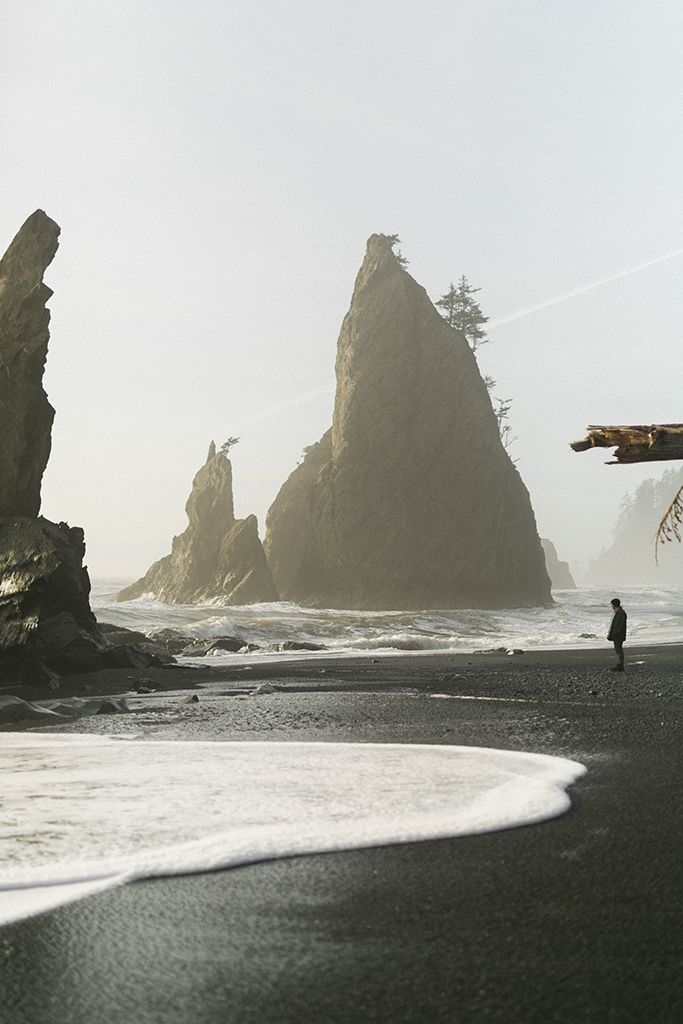 a person is walking on the beach near some large rocks and water in the ocean