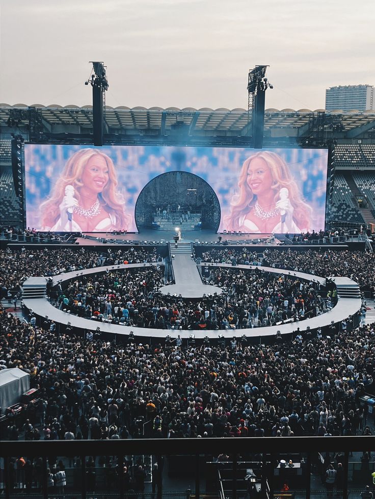 a large crowd at a concert in front of a huge screen with two women on it