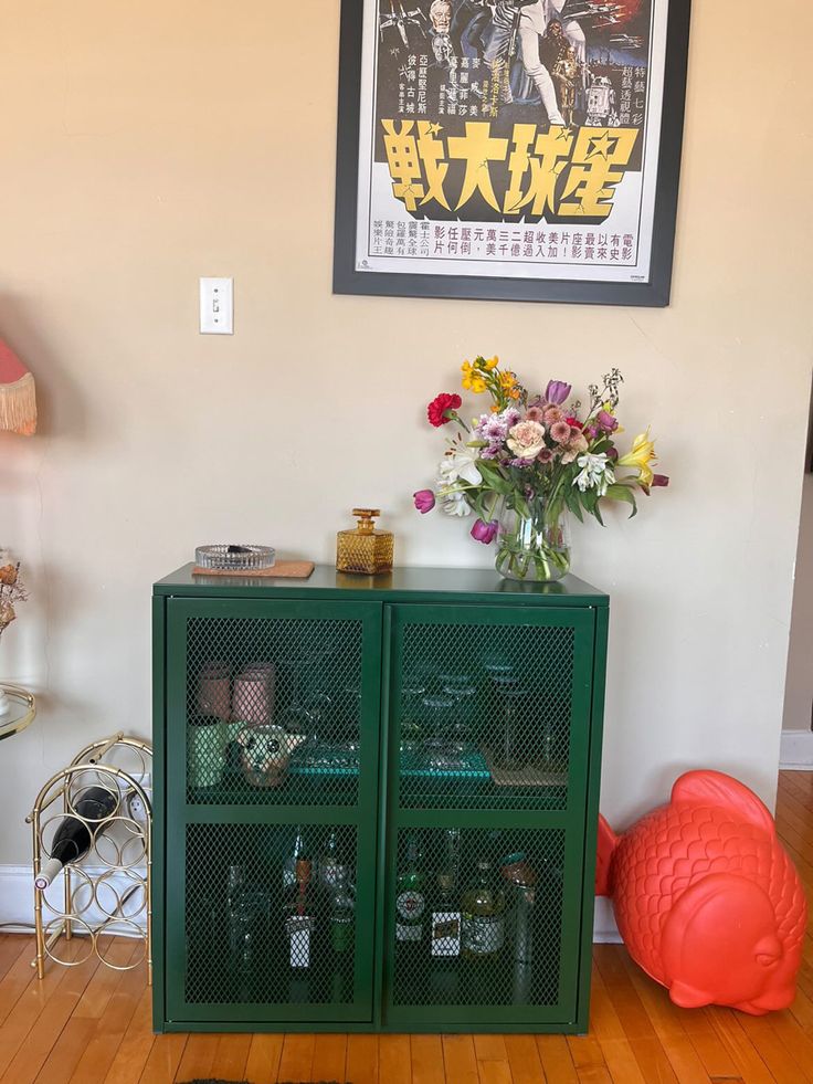 a green cabinet sitting on top of a hard wood floor next to a vase filled with flowers