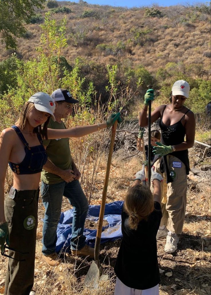 some people are standing in the dirt with shovels and tree sapling tools on their hands