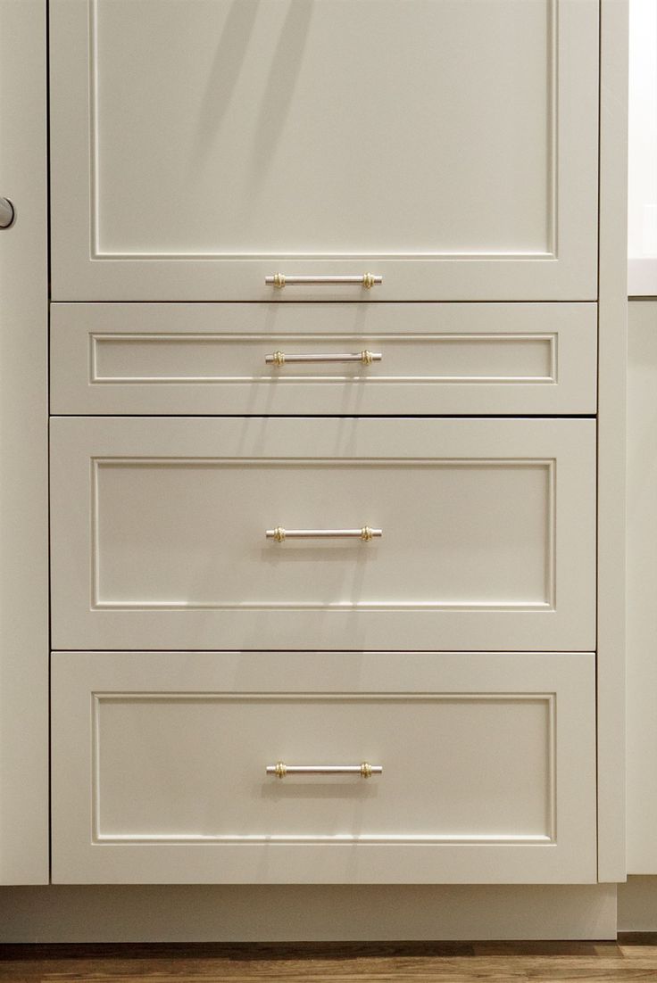 a white cabinet with three drawers and two handles on the bottom, in front of a wooden floor