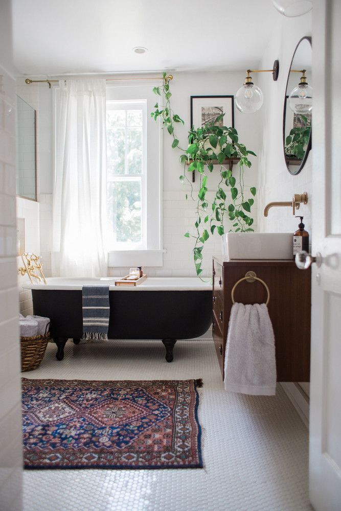 a bath tub sitting next to a sink under a window in a bathroom with a rug on the floor