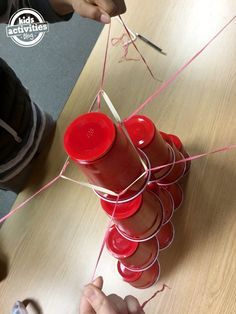 a person is making something out of plastic cups and stringing it with red yarn