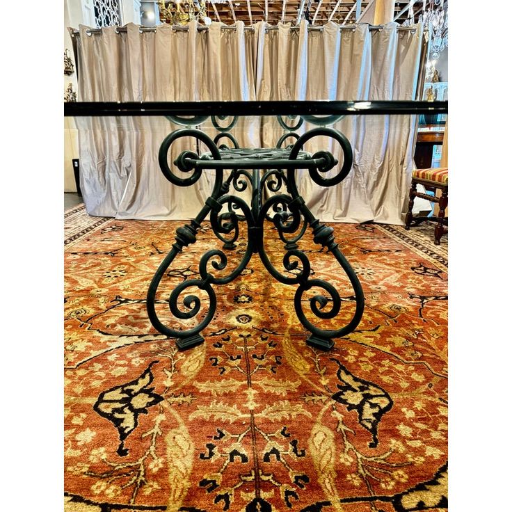 a wrought iron table sitting on top of an orange rug in front of curtained windows