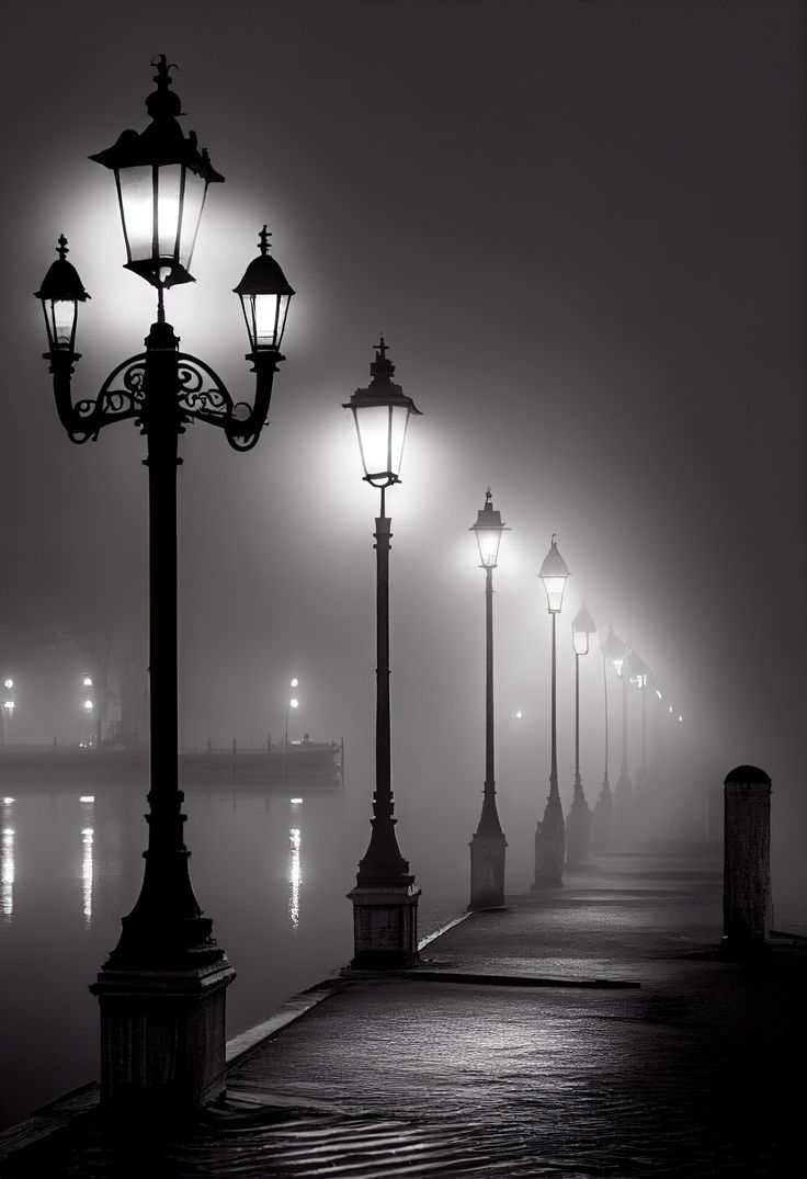 a foggy night with street lamps and lights on the pier in black and white