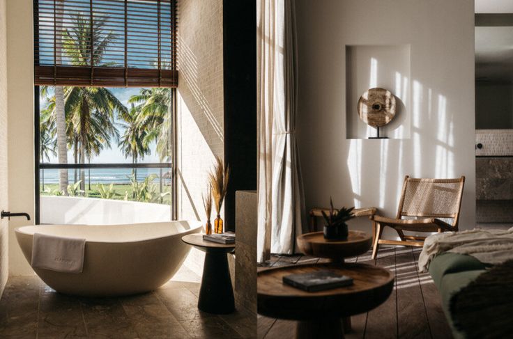 a bath tub sitting in the middle of a bathroom next to a window with palm trees