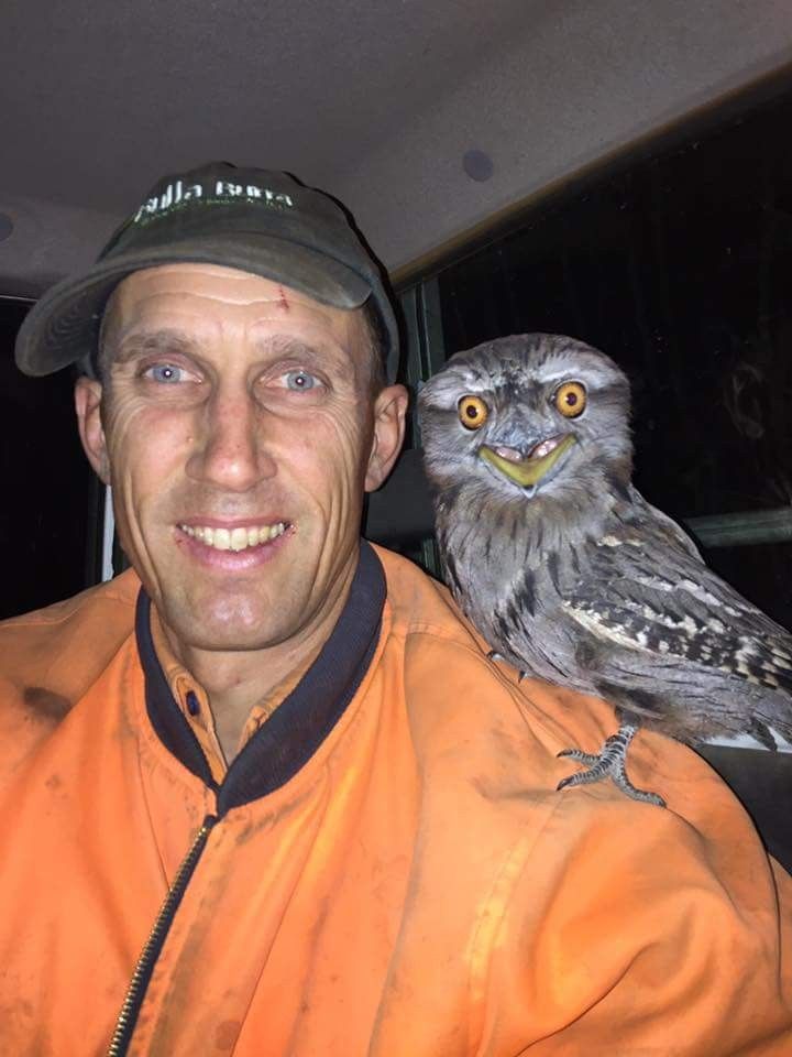 a man with an owl on his shoulder is smiling at the camera while he stands next to him