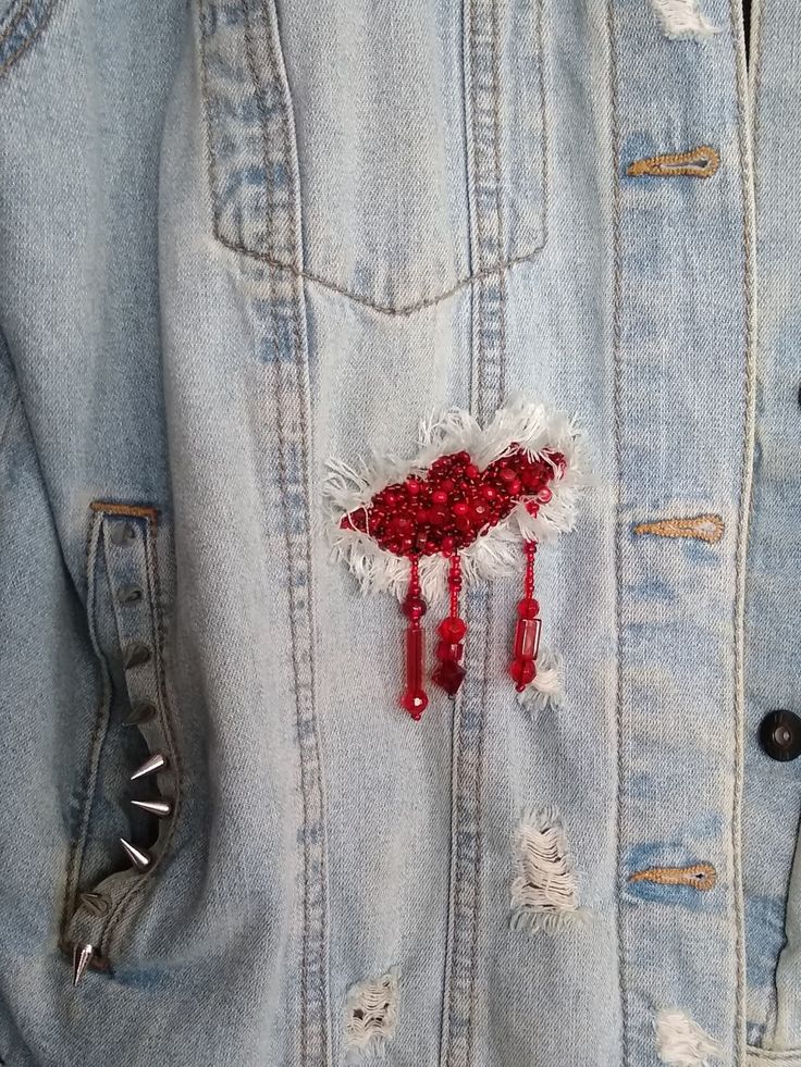 a denim jacket with some red beads hanging off it's back and on the pocket