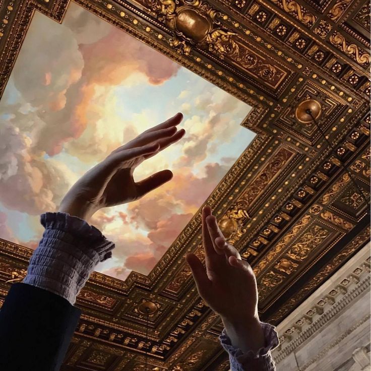 two hands reaching up into the sky above a ceiling with clouds and gold paint on it