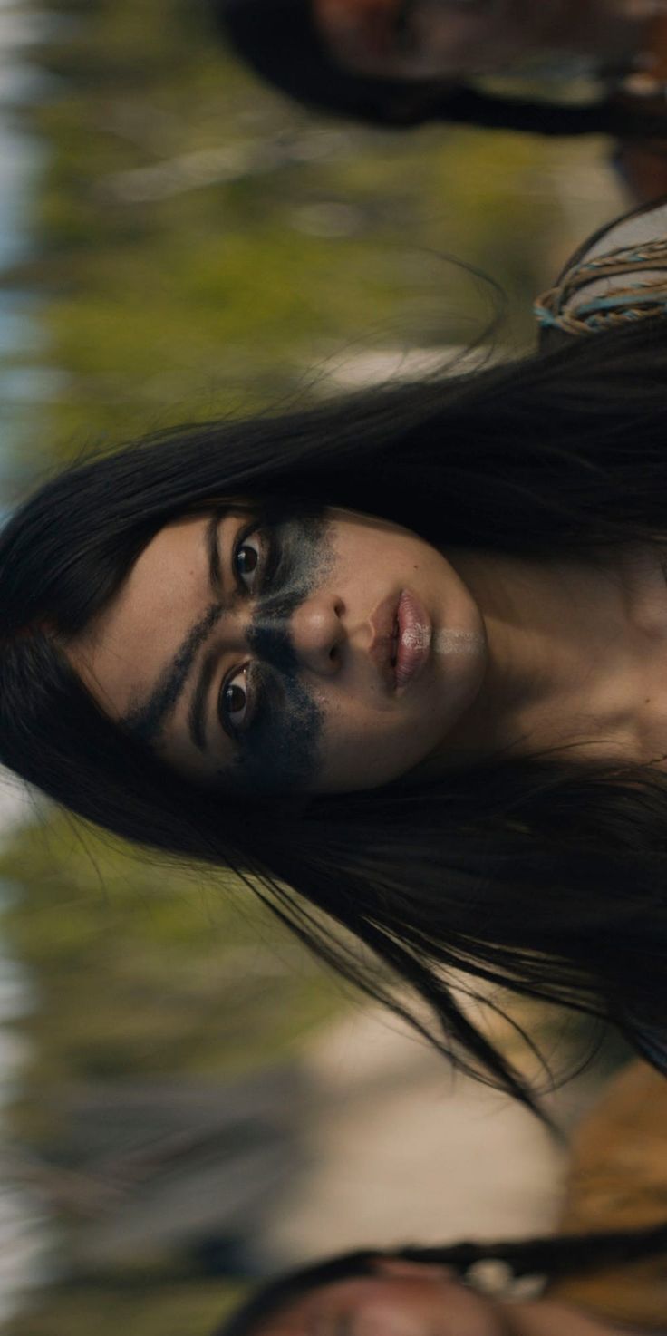 a woman with long black hair standing in front of water