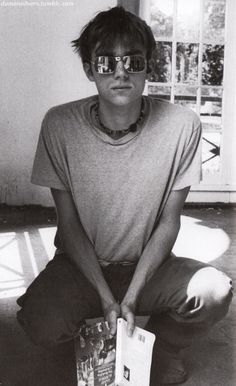 a young man sitting on the floor with his book in front of him while wearing sunglasses