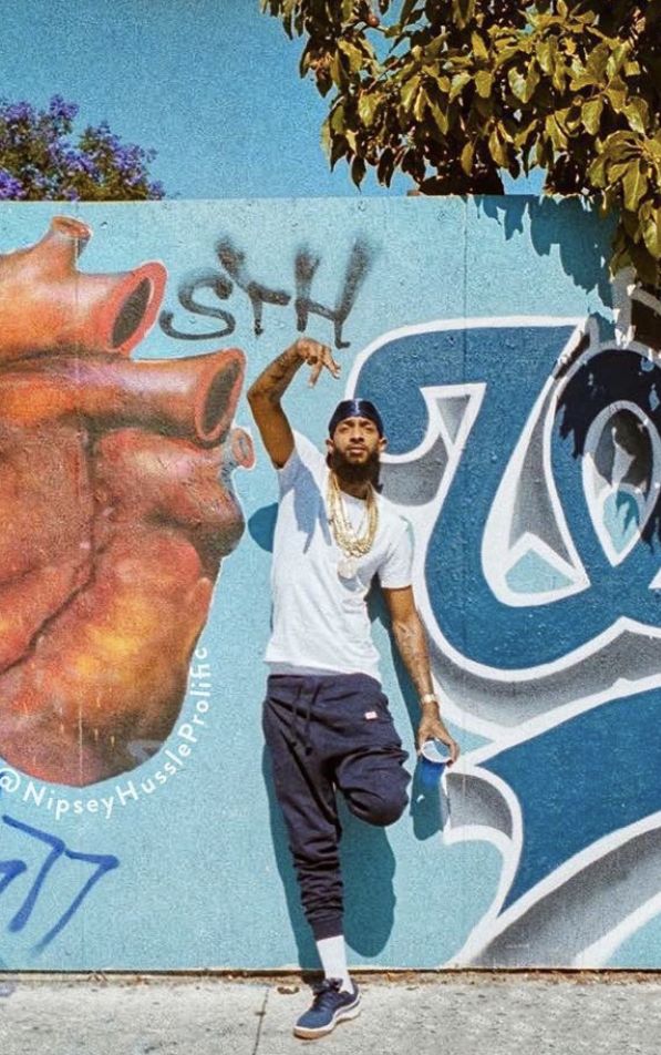 a man standing in front of a wall with graffiti on it and his skateboard