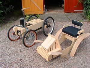 two children's wooden pedal cars sitting on gravel