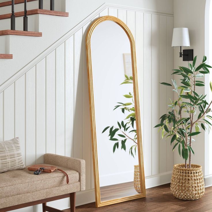 a large mirror sitting on top of a wooden floor next to a plant in a vase