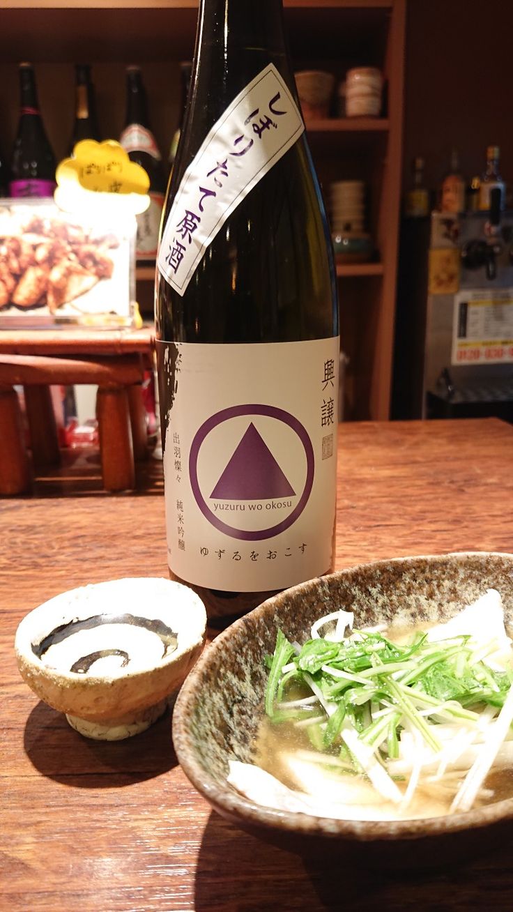 a bottle of wine sitting next to a bowl of food on top of a wooden table